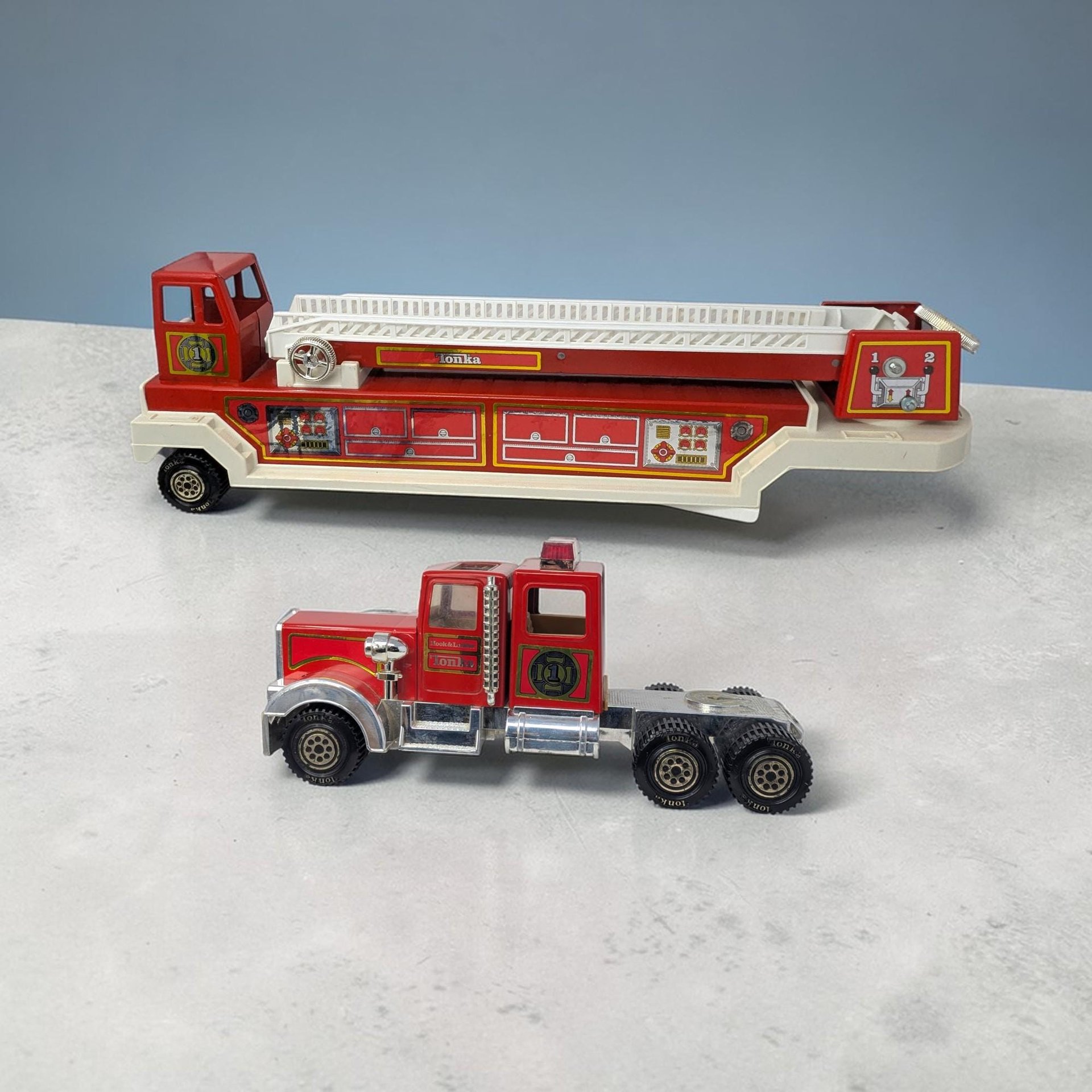 A 33-inch two-piece red Tonka fire truck with a long horizontal silhouette and a hard metal and plastic texture. It features a white extendable ladder, silver-tone cab accents, and small star-shaped sticker remnants on the body.