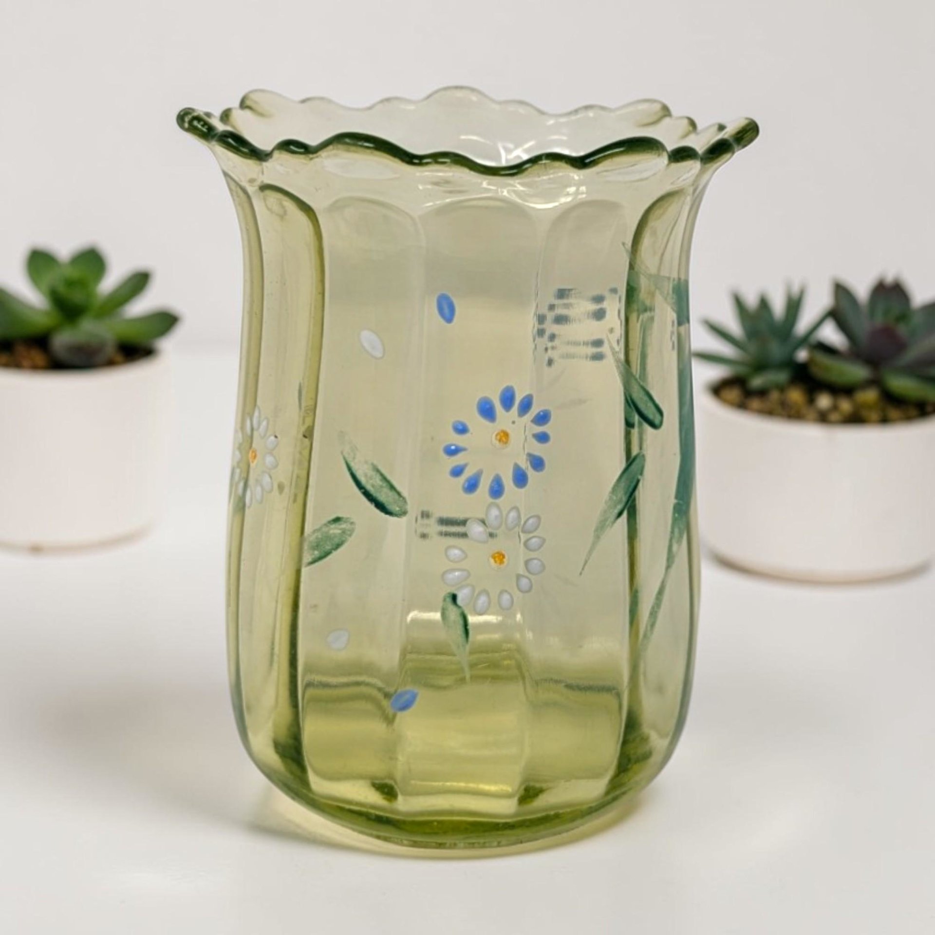 Scalloped rim green glass vase with vertical ribbing and hand-painted blue and white flowers with green leaves.