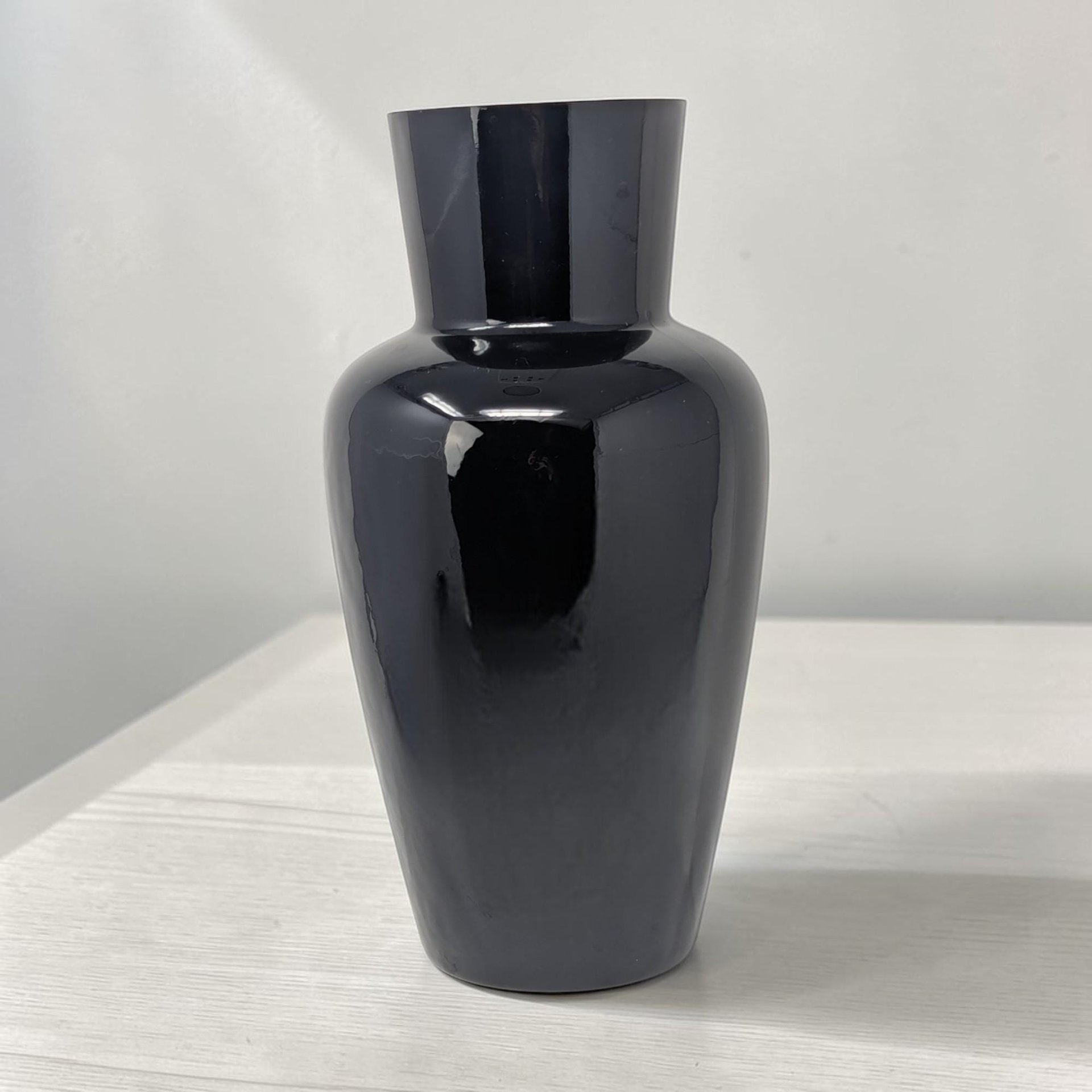 Tall, opaque black glass vase with a high-gloss finish. It features a wide, rounded shoulder tapering down to a narrow base and up to a flared rim. Smooth, reflective surface with no external patterns.