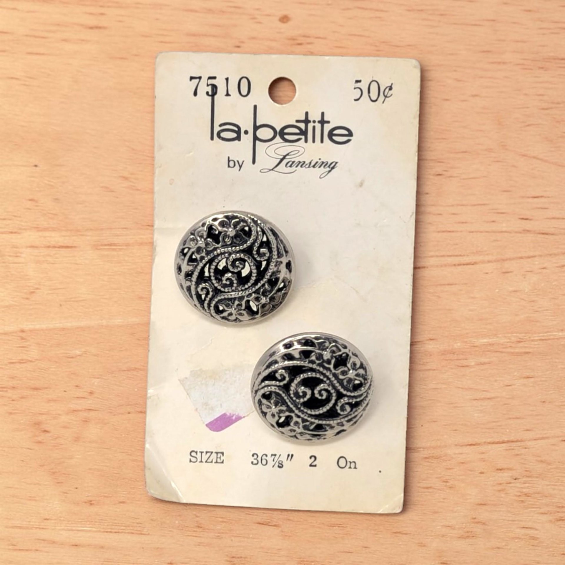 Two circular silver tone buttons on a white card. The buttons feature an intricate openwork filigree design with swirling patterns and beaded textures. They have a high-shine metallic finish and a domed silhouette.