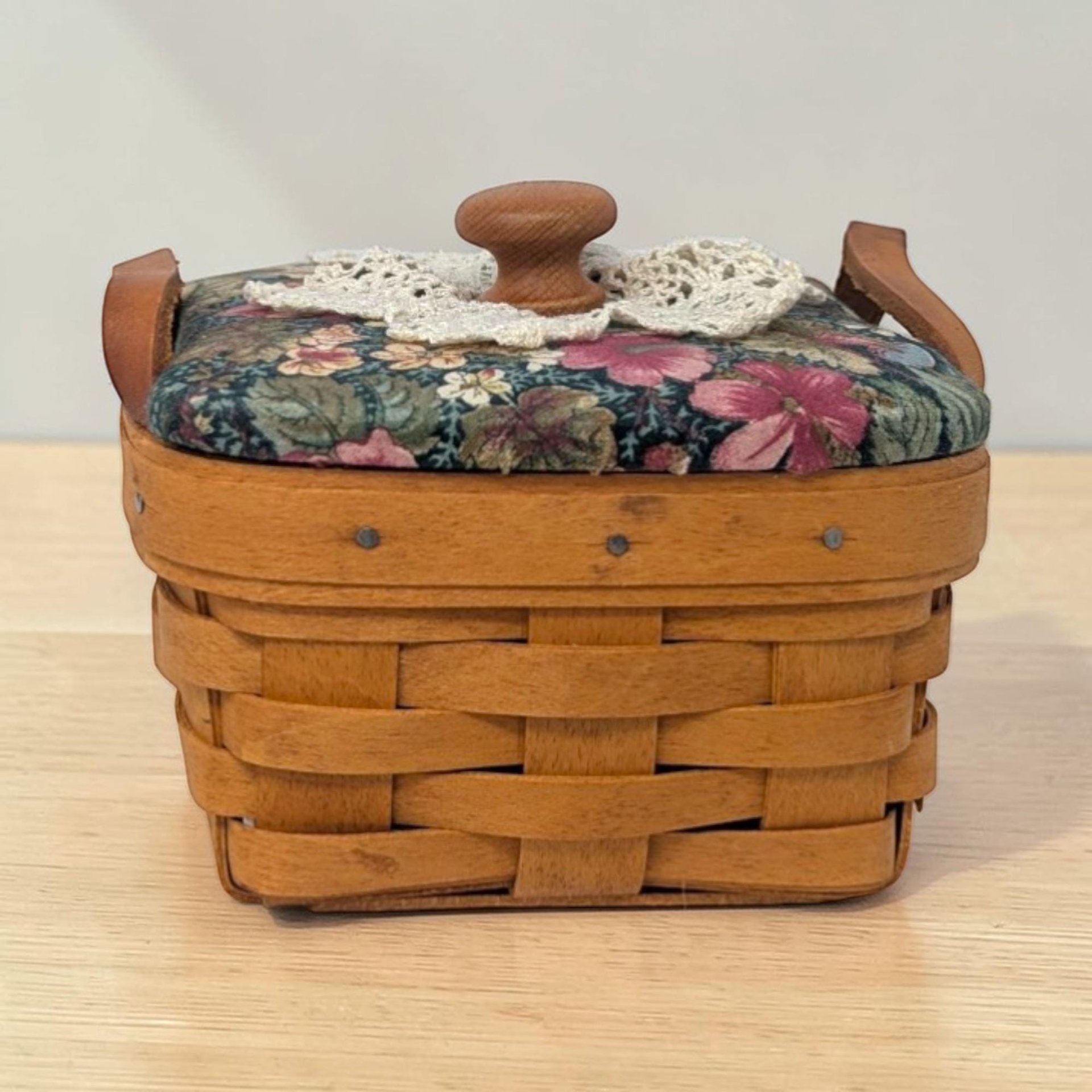 A small square woven maple wood basket with a single swinging handle. The weave features a single green horizontal accent strip near the top rim. The base is solid wood and the interior is unlined.