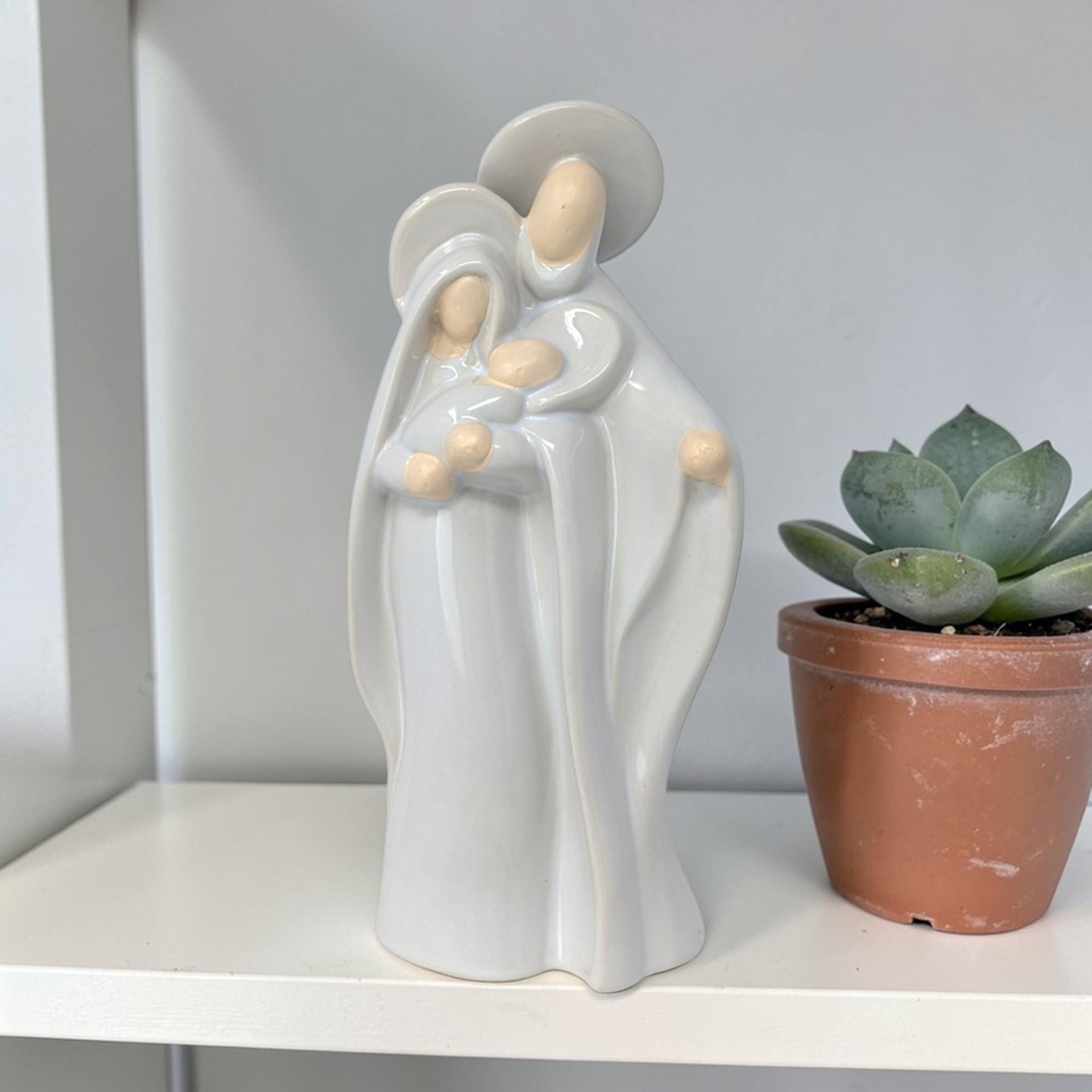 A tall ceramic statue of Mary, Joseph, and the infant Jesus. The texture is a smooth, high-gloss white glaze with a vertical, tapered silhouette and a flat base.
