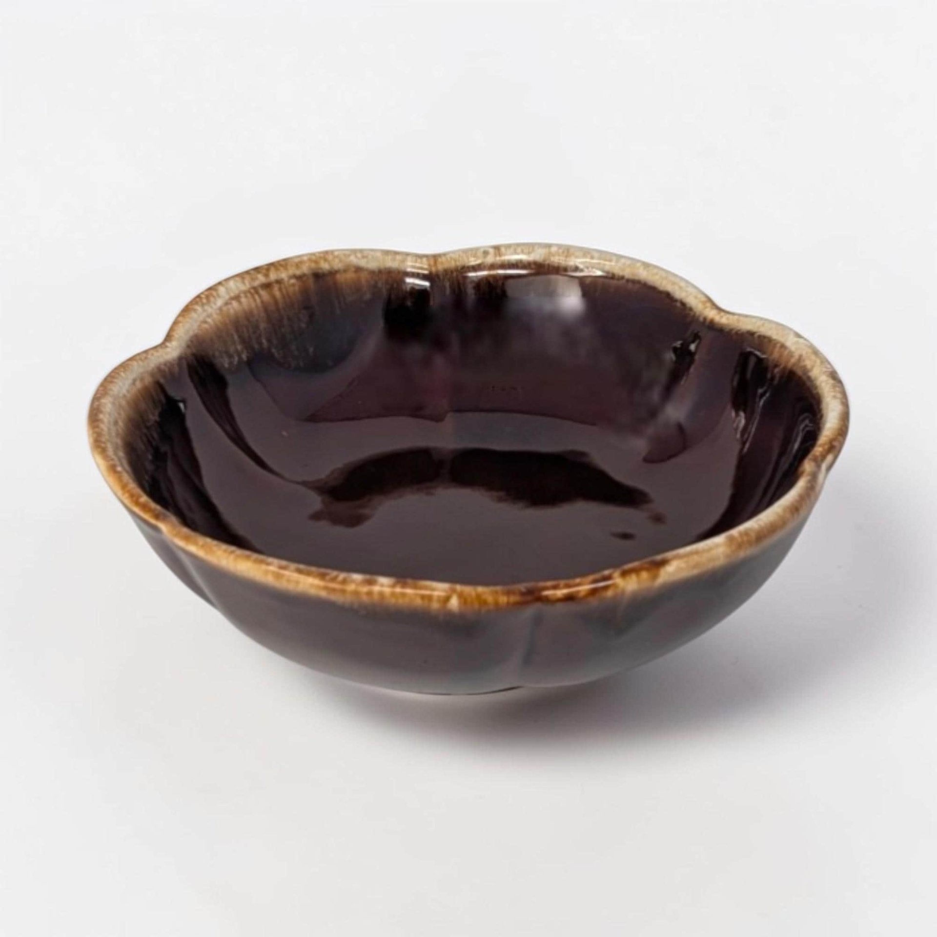 A shallow, round ceramic bowl with a rich dark chocolate brown glaze. A thick, frothy cream-colored drip effect rings the smooth top edge, flowing downward toward the center in an organic pattern.