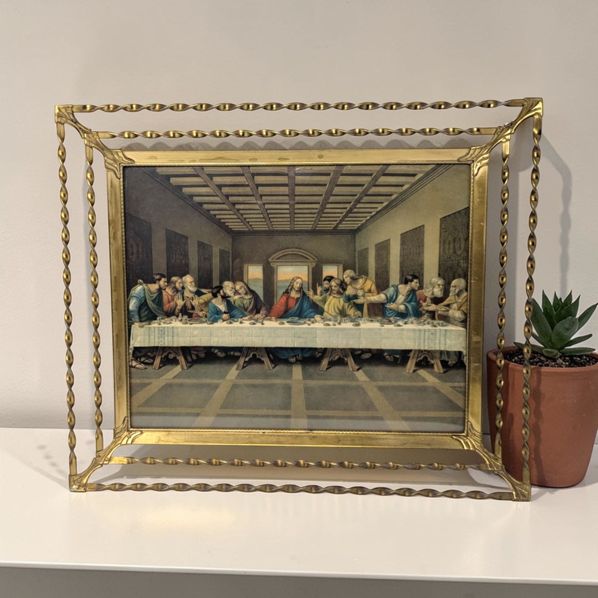 A 12 by 10.5 inch framed Last Supper print with a rectangular silhouette and a metallic twisted wire texture. The gold-tone frame features a unique double-layered openwork design around the central religious lithograph.