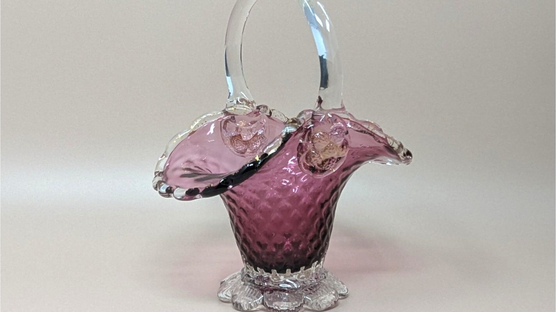 A vibrant cranberry pink glass basket with a clear arched handle. The body features a raised hobnail texture and a ruffled, flared rim, supported by a clear, scalloped pedestal base.