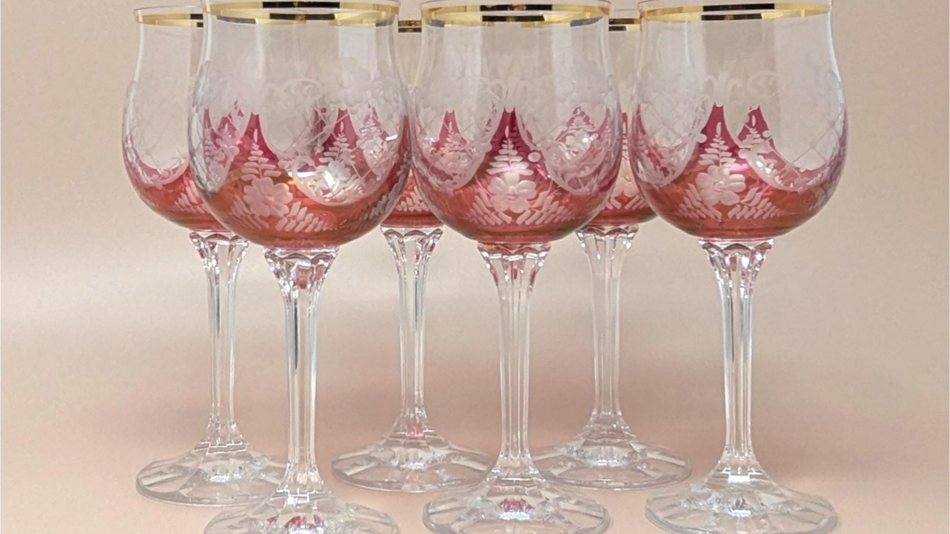 A set of six wine glasses with cranberry red bowls featuring frosted etched floral patterns and gold rims. The stems are tall, clear, and multi-faceted with a flat circular base.