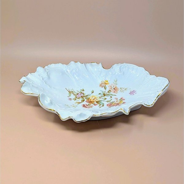 Large, ornate Carl Tielsch porcelain bowl with a highly ruffled, scalloped edge and gold gilt trim. Features embossed scrollwork and a central transfer of autumnal wildflowers in peach, pink, and yellow.