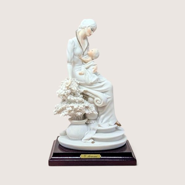 Vintage 1992 Giuseppe Armani porcelain figurine of a mother and child seated next to a floral sculpture on a wooden base.