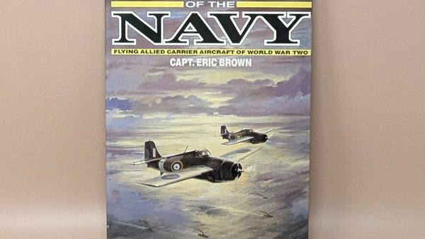 Hardcover book titled "Wings of the Navy" by Capt. Eric Brown. Dust jacket features a painting of two Allied fighter planes flying over a sunset-lit sea. 1987 edition.