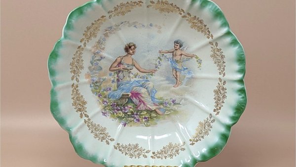 Antique Dresden porcelain bowl with a scalloped edge and green ombré rim. Center features a classical scene of a woman and a cherub with floral garlands. Gold filigree accents. 9.25 inches wide.