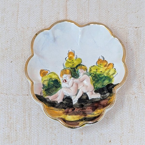 Scalloped Capodimonte porcelain trinket dish with a high-relief embossed scene of two children in a garden. Hand-painted in earthy tones with a gold gilt rim. 5.5 inches wide.