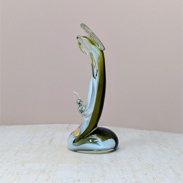 A vertical art glass sculpture of a person in a prayerful pose. A vibrant green inner layer is visible through the thick clear glass exterior, which curves into a stable, weighted base.