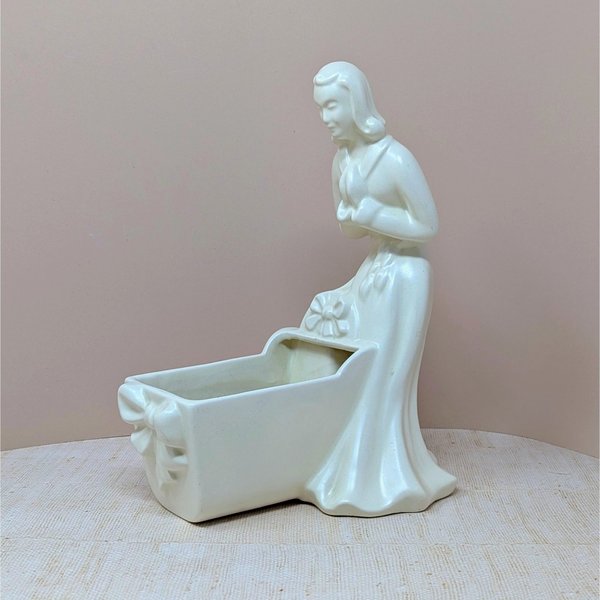 Vintage Royal Haeger white pottery planter featuring a colonial-style woman in a flowing dress leaning over a baby cradle. High-gloss "Alabaster" white glaze. 11 inches tall.