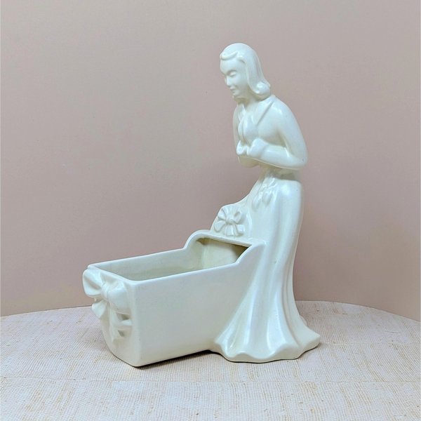 Vintage Royal Haeger white pottery planter featuring a colonial-style woman in a flowing dress leaning over a baby cradle. High-gloss "Alabaster" white glaze. 11 inches tall.