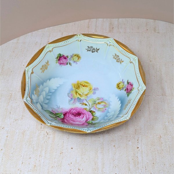Scalloped octagonal porcelain bowl. Pale blue ombre interior with large pink and yellow roses. Wide rim features heavy gold gilt with a delicate beaded relief texture.