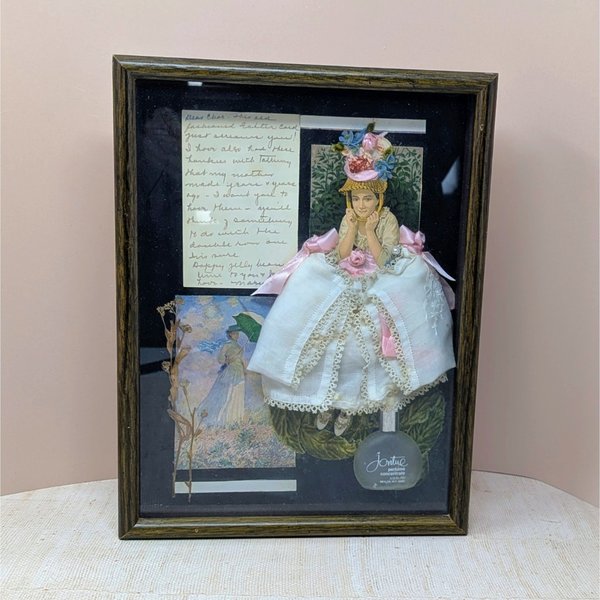 Dark wood shadow box featuring a 3D collage of a Victorian woman in a white lace dress. Black background with a frosted perfume bottle, dried botanicals, and handwritten yellowed paper. Rich, layered multimedia textures.