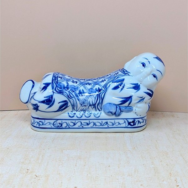 A horizontal porcelain headrest shaped like a reclining child. Featuring a crisp white ground with traditional cobalt blue floral and scroll patterns. Glossy vitrified texture with hand-painted facial details.