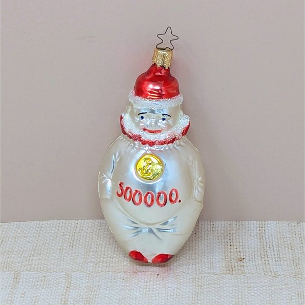 A vertical 5.5-inch blown glass clown ornament with a silvered body. The clown wears a red hat and ruff, with a gold medallion on its chest and "500,000" painted in red across the belly. Topped with a signature star-shaped metal cap.