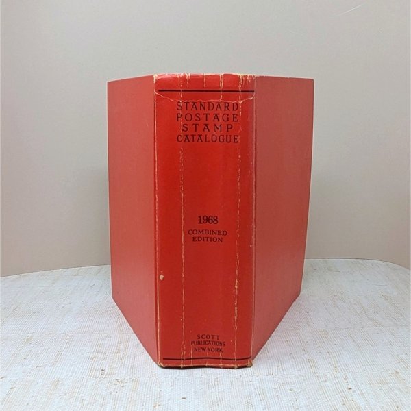 A thick, red hardcover book with a textured spine. The text reads Standard Postage Stamp Catalogue 1968 Combined Edition in black ink. The cover shows gentle edge wear and a slight lean from its substantial page count.