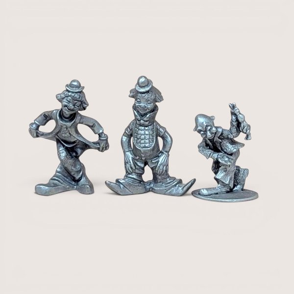 A trio of vintage silver-toned pewter clown figurines. One is in a deep curtsy, another is mid-stride in a classic circus pose, and the third is a dapper clown with a tall hat and buttons. Each figure has a matte metallic finish with fine sculptural details.
