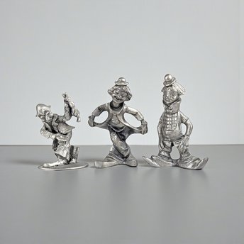 A set of three vintage silver-toned pewter clown figurines in different poses, including one bowing in a curtsy, one standing with hands in pockets, and one in a playful walking stance.