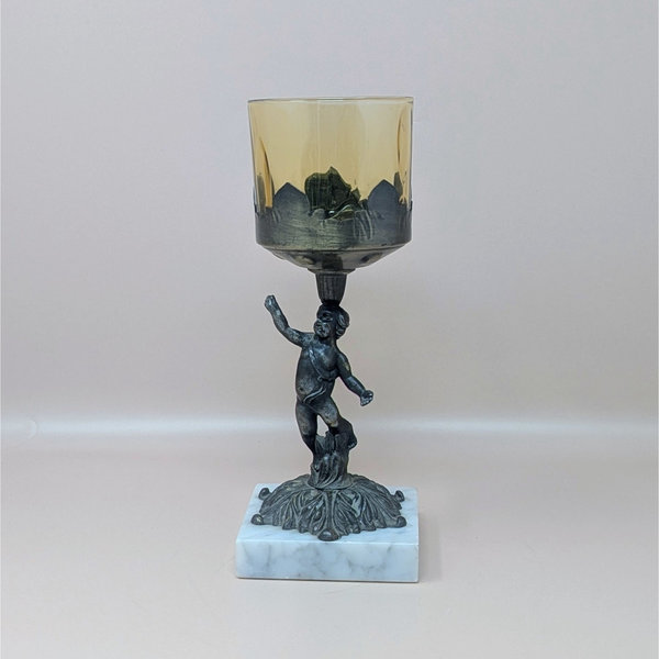 A 9-inch vintage candle holder featuring a dark cast metal cherub figure standing on a white marble square base, supporting a translucent amber glass cup.
