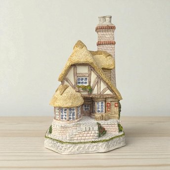 A highly detailed David Winter miniature sculpture of a two-story timber-framed cottage with a thick thatched roof, cobblestone base, stone chimney, and hand-painted floral accents.