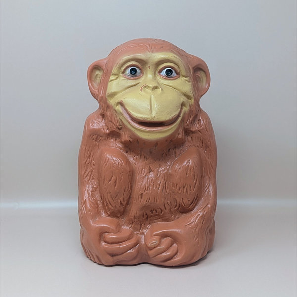 A large, light-brown molded plastic monkey bank with a tan face and a wide grin, standing against a neutral background.