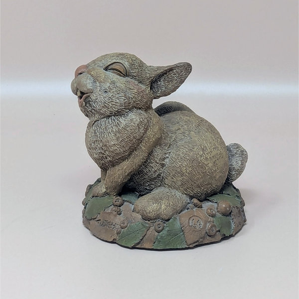 A hand-painted resin sculpture of a rabbit named Twitch scratching its ear on a mossy, leaf-strewn base against a neutral background.