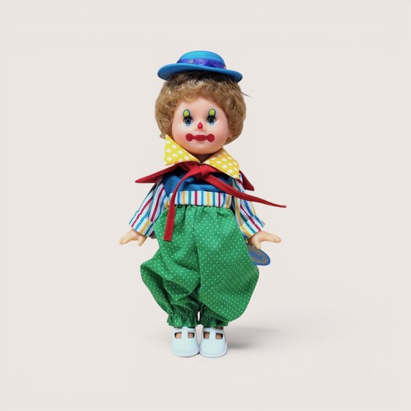 A vintage 10-inch Horsman clown doll with brown hair and a blue hat wearing a colorful mismatched outfit of stripes and polka dots against a neutral background.
