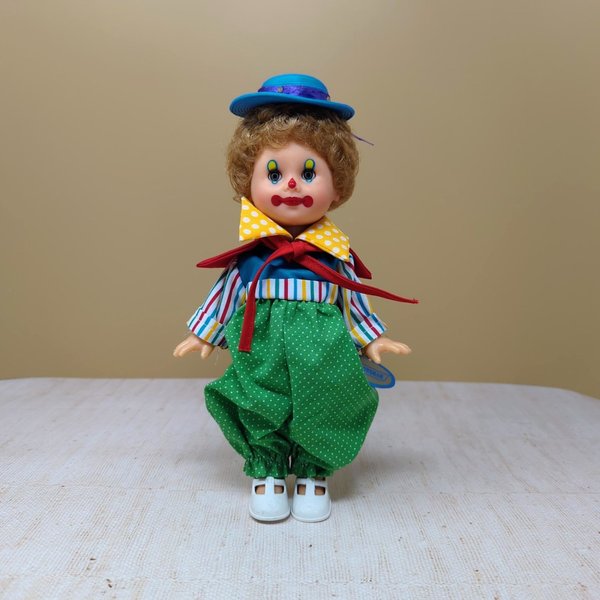 A vintage 10-inch Horsman clown doll with brown hair and a blue hat wearing a colorful mismatched outfit of stripes and polka dots against a neutral background.