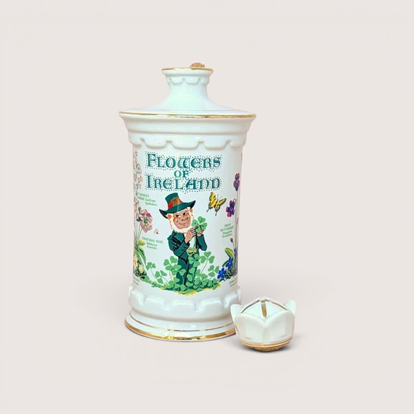 A white porcelain decanter featuring botanical "Flowers of Ireland" illustrations, a leprechaun figure, and a gold-trimmed flower-shaped stopper against a neutral background.