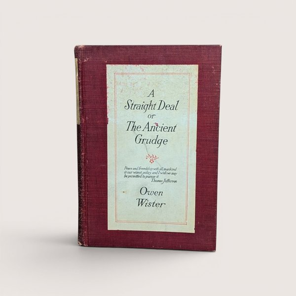 An antique book titled A Straight Deal or The Ancient Grudge by Owen Wister with a maroon cloth cover and cream paper label.