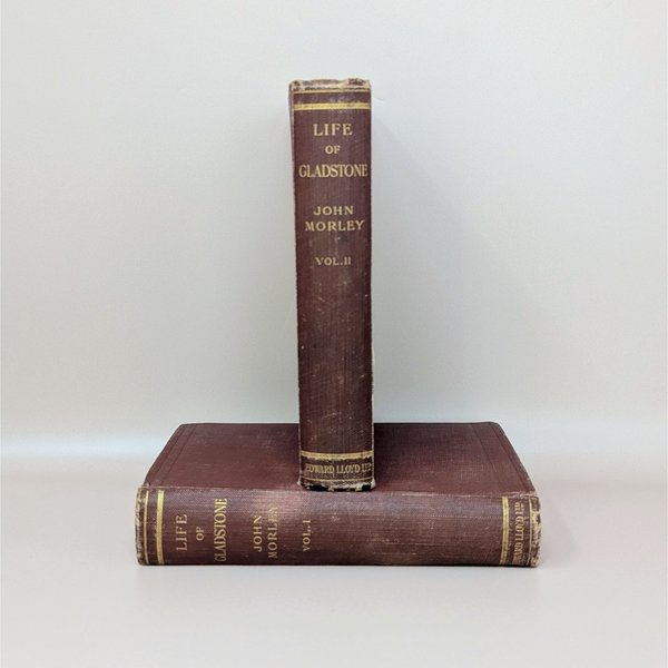Two antique burgundy cloth-bound books stacked horizontally, showing gilded spine titles for The Life of Gladstone by John Morley.