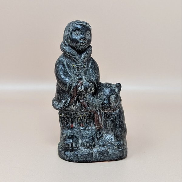 vintage black resin figurine depicting an Eskimo child in a fur-trimmed parka standing next to a large dog, featuring hand-painted red and blue details on the garment over a neutral tan background.