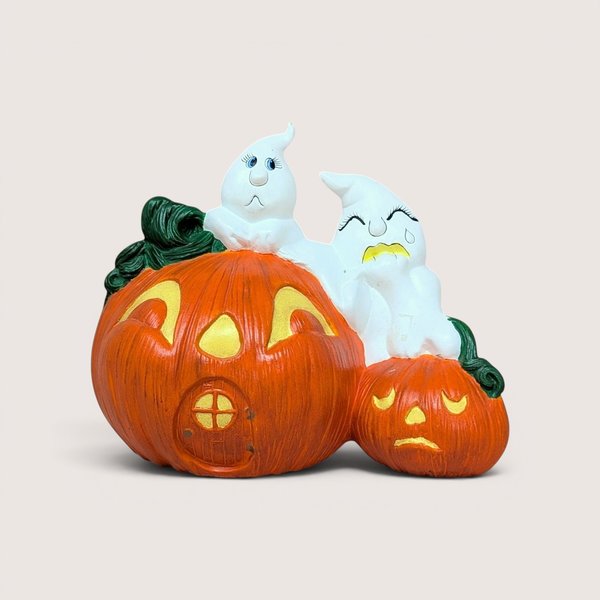 A vintage hand-painted ceramic figurine featuring two white ghosts perched atop a large orange jack o' lantern house and a smaller sad pumpkin.