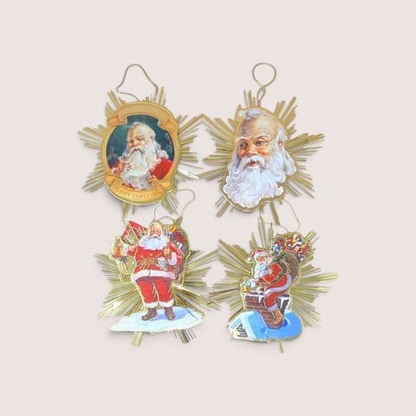Four vintage paper illustration Santa Claus ornaments with reflective gold tinsel starburst backings on a light background.