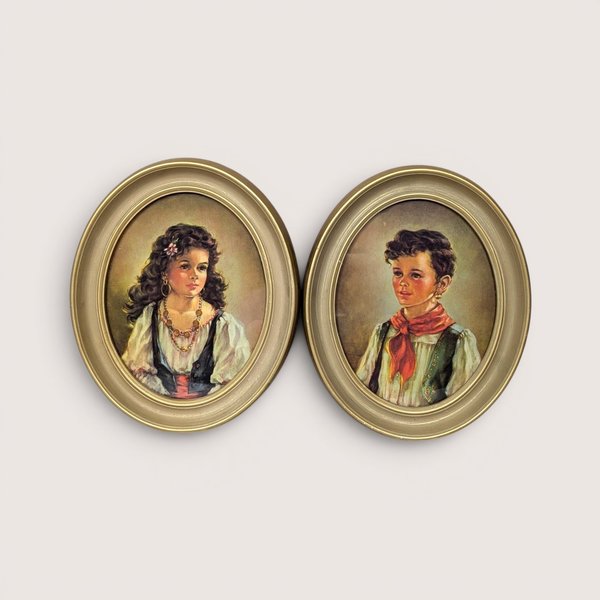 A pair of 1950s vintage Ann Allaben framed oval prints on a tan textured background. The matching set features the portraits of a young Spanish girl named Elena and a boy named Chico, both dressed in traditional mid-century clothing inside gold oval frames.