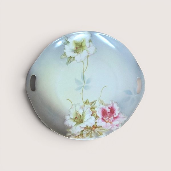 A round porcelain handled plate with painted pink and white floral details, centered on a beige background.