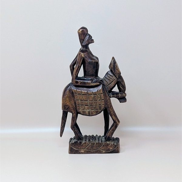 A vintage hand carved dark wood sculpture of an African woman riding a horse with a textured base
