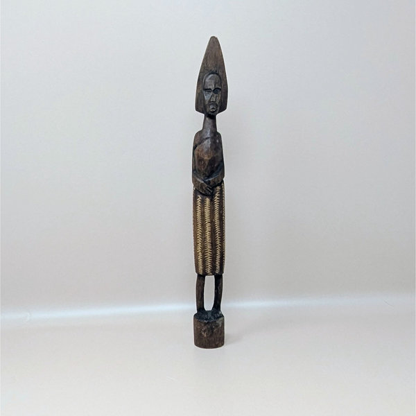 A vintage slender hand carved dark wood African figurine with a tall pointed headdress and a textured patterned skirt