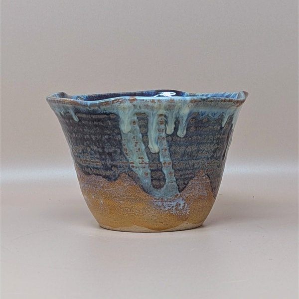A vintage hand thrown studio pottery bowl featuring deep blue and light blue drip glazes over an unglazed sandy brown base