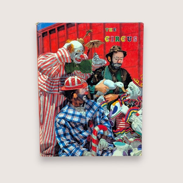 A 1961 vintage Ideals Publication book titled The Circus on a Dune colored background. The hardcover front features a vibrant red illustration of mid-century circus clowns in colorful striped and plaid costumes gathered together with a white duck.