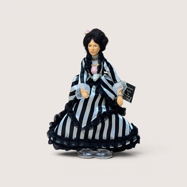 A vintage Peggy Nisbet costume doll in a black and white striped gown with ruffles, centered on a beige background.