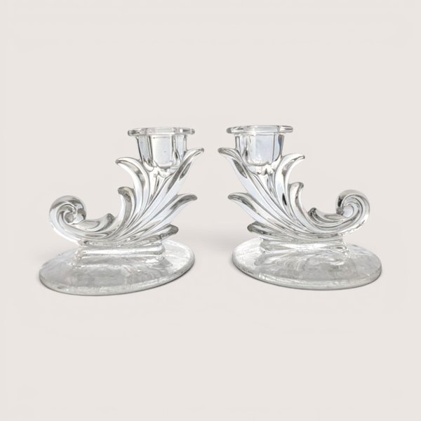 A pair of vintage clear glass cornucopia or leaf-shaped single candlestick holders, centered on a beige background.