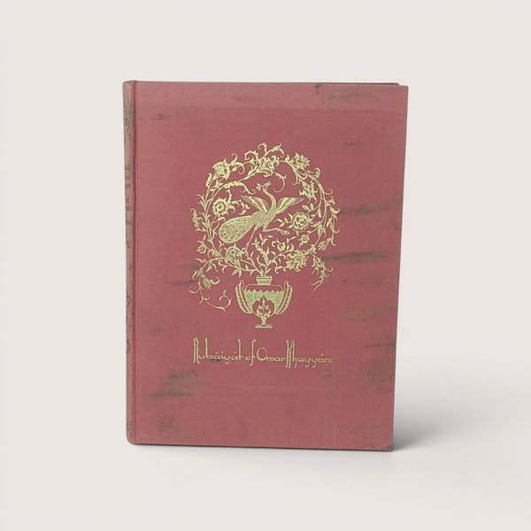 A vintage rose pink cloth hardcover book featuring a gold gilt peacock medallion on the front cover