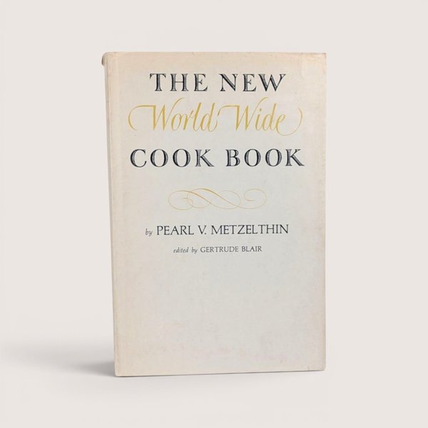 Vintage cookbook titled The New World Wide Cook Book by Pearl V Metzelthin centered on a plain linen background.