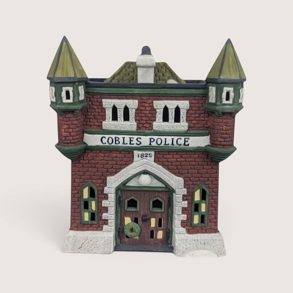 Dept. 56 Cobles Police Station ceramic building with a red brick facade and twin green turrets on a plain background.