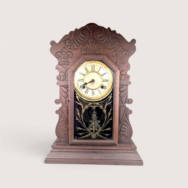 Antique Waterbury Tampa gingerbread parlor clock with an intricately carved walnut case and gold stenciled glass door.