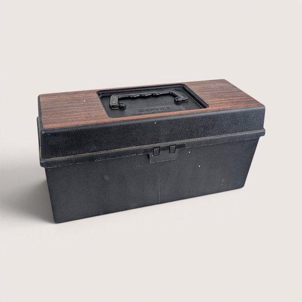 A vintage black plastic Service 8-track carrying case filled with a collection of retro music cartridges.